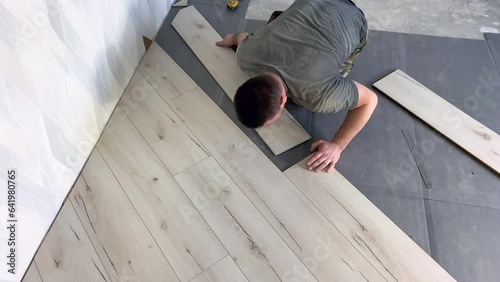 Laying a gray parquet board on the substrate. The work of a builder. A man repairs the floor in the room. The process of laying laminate on a polyurethane substrate. Floor repair. High quality 4k