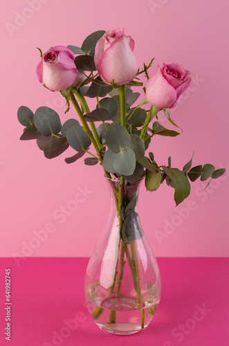 Vertical image of pink rose flowers in glass vase and copy space on pink background