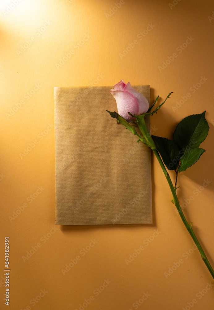 Fototapeta premium Vertical image of pink rose flower on brown paper and copy space on orange background