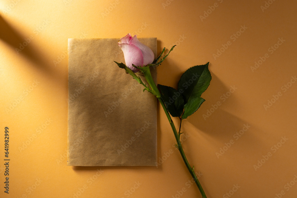Naklejka premium Pink rose flower on brown paper and copy space on orange background