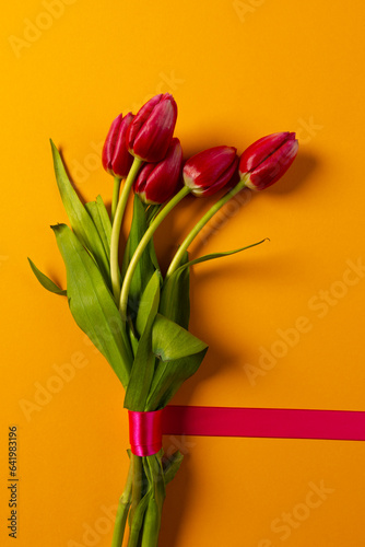 Vertical image of bunch of red tulips with red ribbon and copy space on orange background