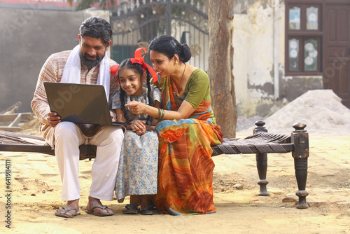 Schilderij op canvas Happy Indian Rural family sitting on cot outside with girl child