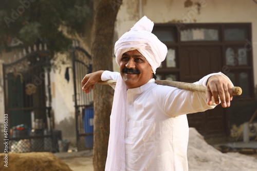 Mid-Aged man in Rural Environment wearing kurta-pajama which is traditional Dress for men in North India in day time holding walking cane. photo