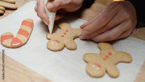 Homemade gingerbread cookies in the shape of little people for Christmas, the woman decorates them with icing.