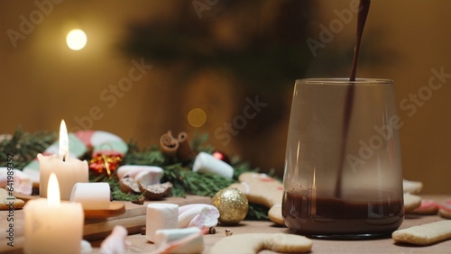 Christmas table with sweets and candles along with other decorations. Gingerbread cookies are scattered across the table. Hot cocoa is being poured into a mug.