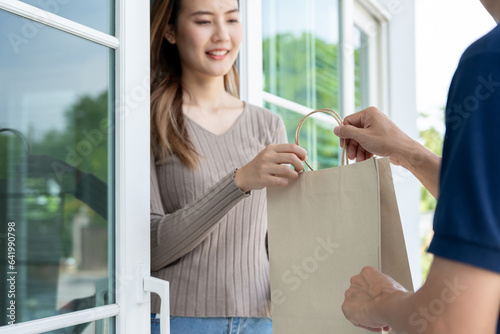 Billede på lærred Happy smiling Asian woman receives paper bag parcel of food from courier front house