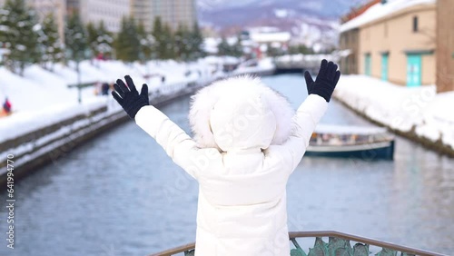 Woman tourist Visiting in Otaru, happy Traveler in Sweater sightseeing Otaru canal with Snow in winter season. landmark and popular for attractions in Hokkaido, Japan. Travel and Vacation concept photo