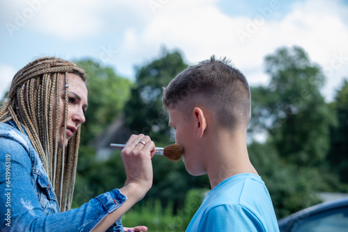 A woman with African braids applies powder to a boy face with a powder brush. Copy space