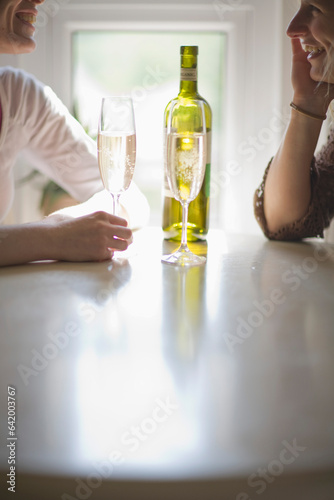 Two young women sitting at table talking laughing and drinking wine
 photo
