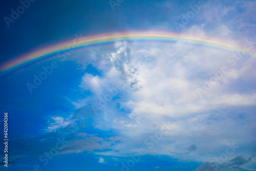 Beautiful multi-colored rainbow after rain on the blue sky and white clouds.
