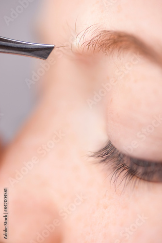 Extreme close up of young woman plucking own eyebrow hair with tweezers
 photo