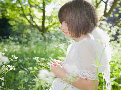 Portrait of young girl in a white fairy costume standing in a garden
