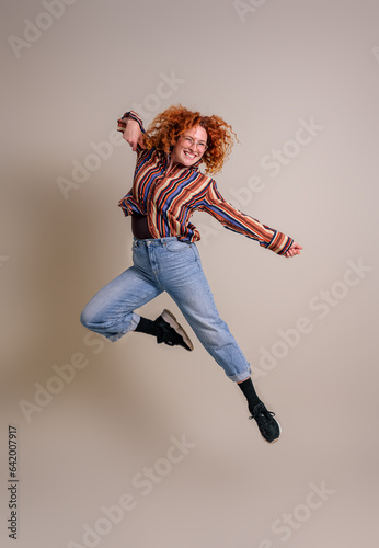 Funky smiling beautiful woman with redhead jumping ecstatically in air against background