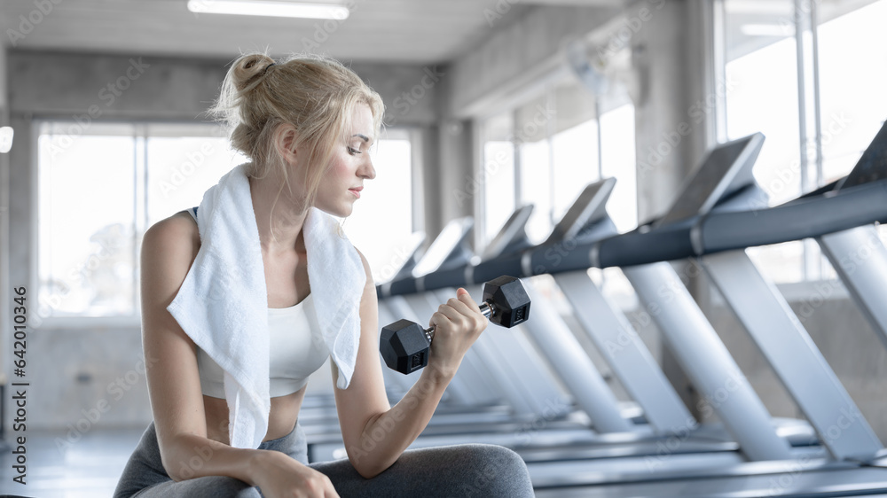 Fototapeta premium Young sport woman exercise with dumbbell at fitness gym. Caucasian girl workout abdominal crunches indoors. Concept of sport, healthcare, physical exercise and beauty shape.