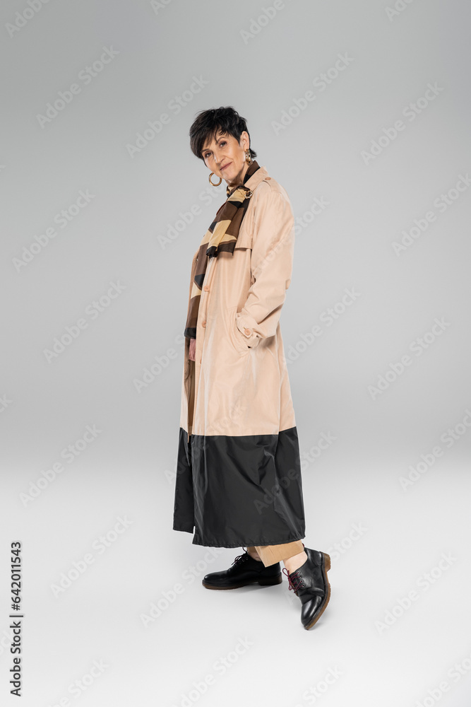 middle aged woman in trendy autumn outfit looking at camera on grey, trench coat, scarf, full length middle aged woman in trendy autumn outfit looking at camera on grey, trench coat, scarf, full length