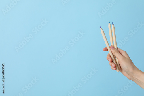 Female hand holds multi-colored pencils on a blue background, place for text
