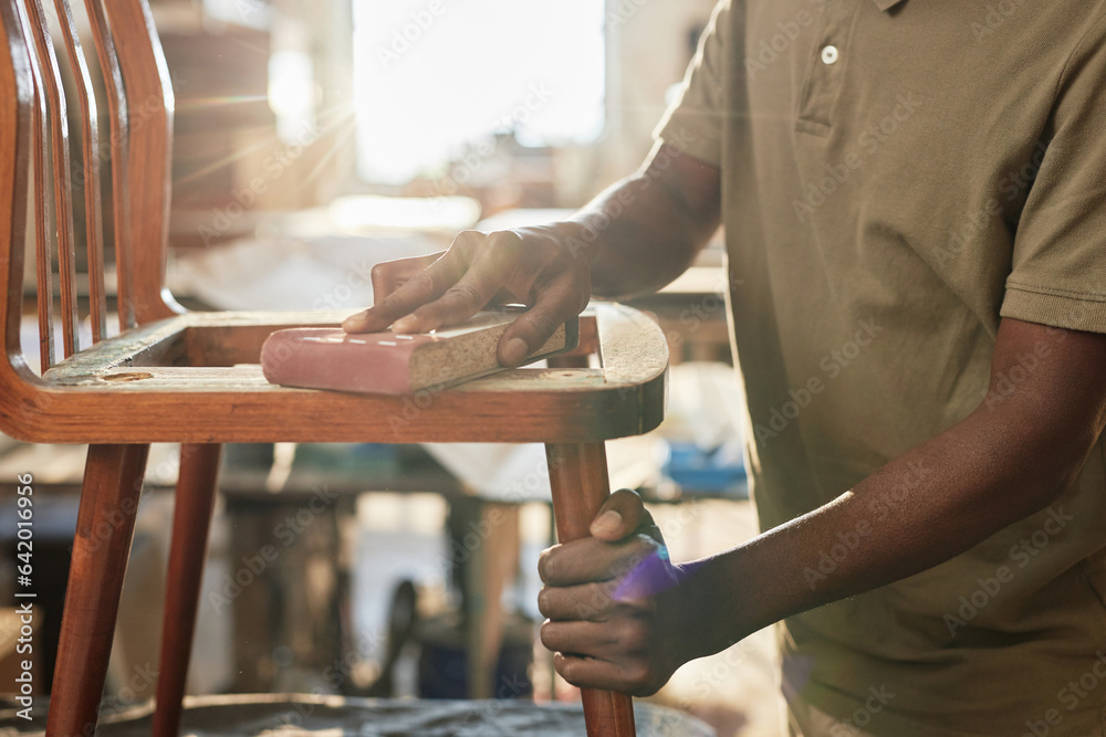 Obraz premium Closeup of black black man polishing old furniture piece in restoration workshop lit by sunlight, copy space