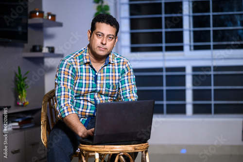 Technology, remote job and lifestyle concept - happy Indian man with laptop computer working at home.