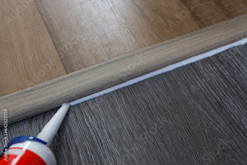 Silicone sealant. Applying silicone caulking on wood floor. photo