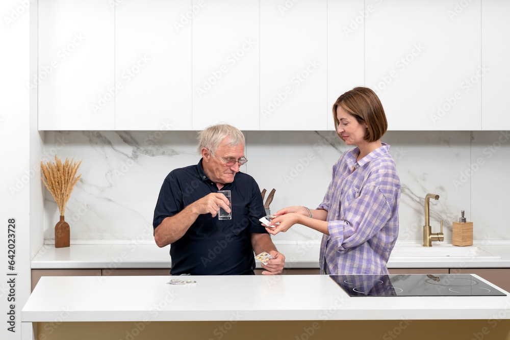 Obraz premium Young woman takes care of an elderly man who is taking medicine. Family relationships and health care concept