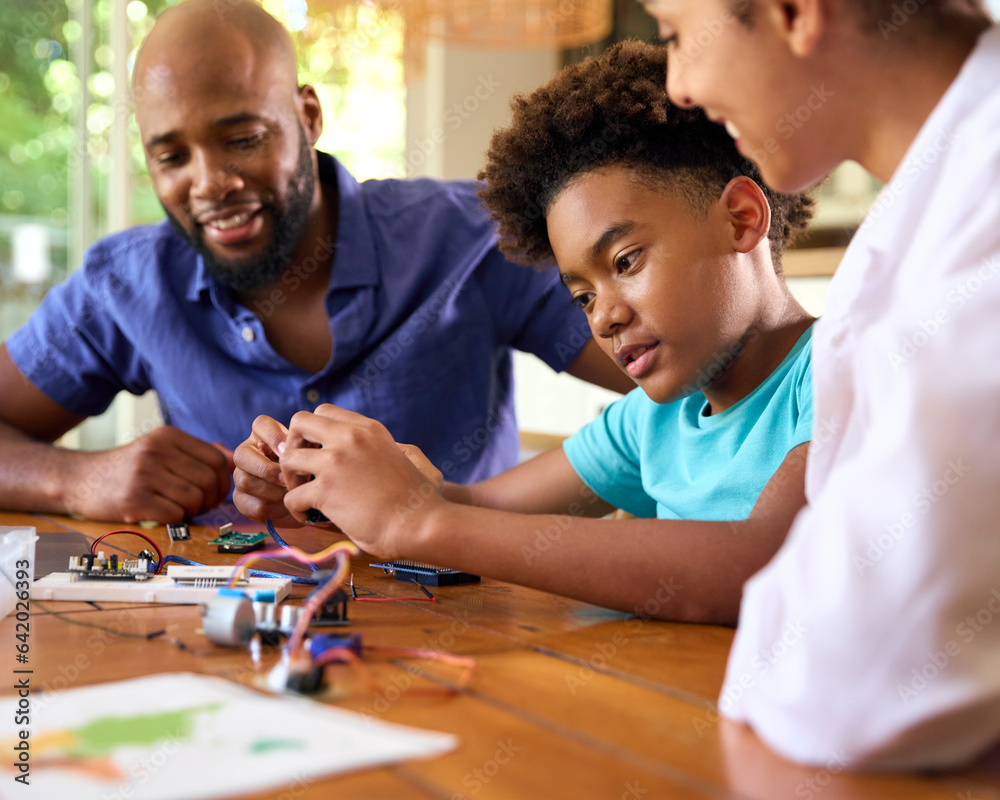 Fototapeta premium Family Around Table At Home Using Laptop With Parents Helping Son With Science Homework