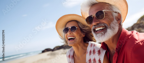 Happy senior couple in hats and sunglasses on the beach on a sunny day. Copy space.