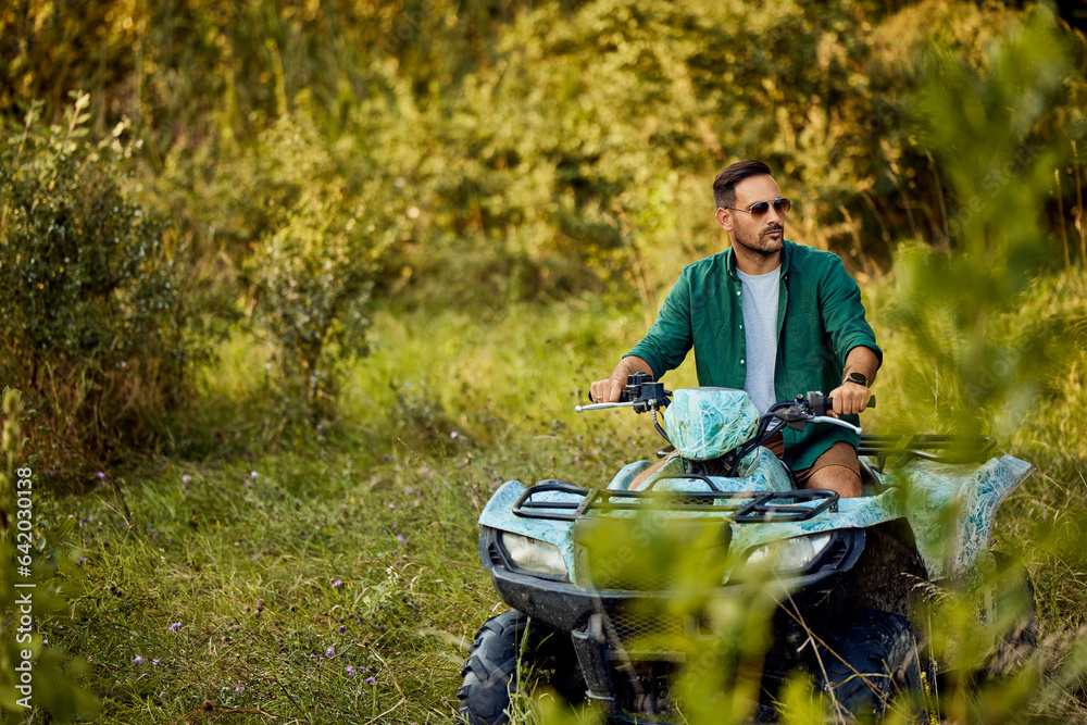 A serious man with sunglasses on driving a rented quad bike through the vegetation.