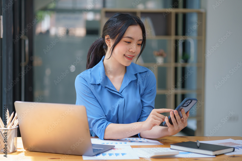 Beautiful businesswoman using a smartphone and working with a laptop while sitting at an office desk, working from home concept. Beautiful businesswoman using a smartphone and working with a laptop while sitting at an office desk, working from home concept.