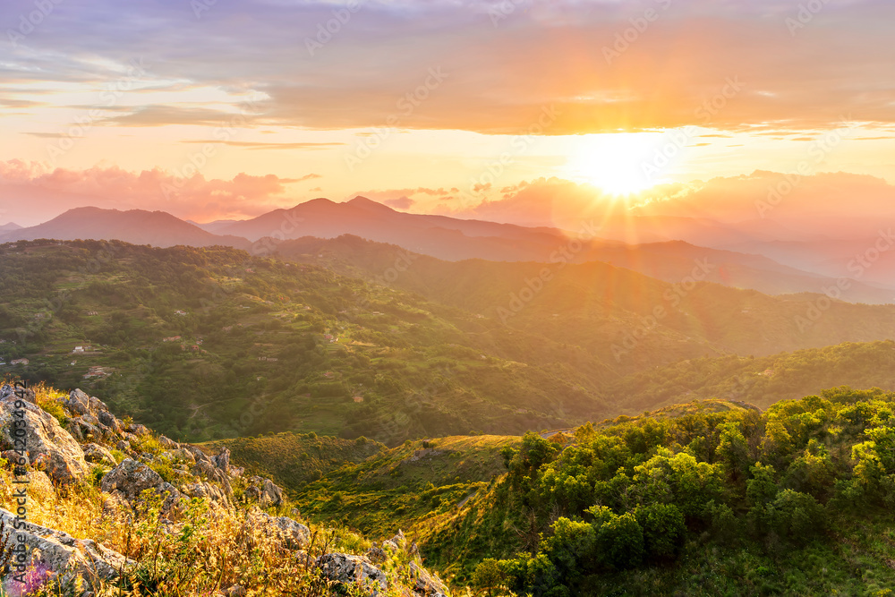 highland mountain landscape of beautiful sunset or sunrise with nice mountain peaks and slopes, green and golden hills and majestic cloudy sky on background