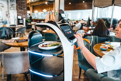 Robot waiter serve food at modern restaurant table.Offering innovation futuristic high-tech automated dining experience.Bringing,delivery automation order to customer.Digital robotic AI smart service