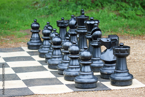 Giant black outdoor chess set pieces on a board photo