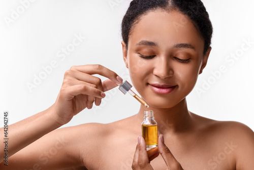 Beautiful woman with bottle of serum and dropper on white background