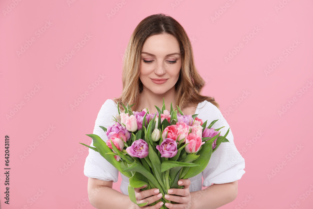 Happy young woman with bouquet of beautiful tulips on pink background