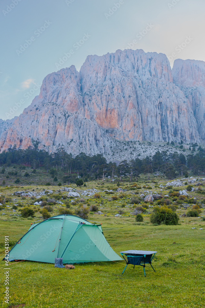 A green camping tent stands on a green meadow with beautiful mountains in the background. Spending time outdoors.