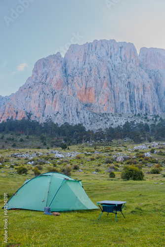 A green camping tent stands on a green meadow with beautiful mountains in the background. Spending time outdoors.