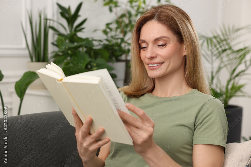 Woman reading book on sofa surrounded by beautiful potted houseplants at home Woman reading book on sofa surrounded by beautiful potted houseplants at home