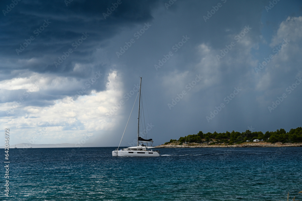 A sailing boat on the sea during storm. Sailboat on water with dark stormy clouds in background. A sailing boat on the sea during storm. Sailboat on water with dark stormy clouds in background.