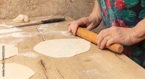 A woman rolls out the dough with a rolling pin on the table
