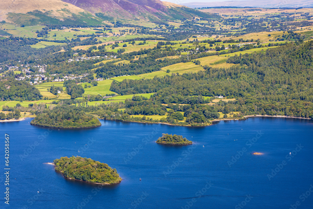 A large lake with small islands and boats, surrounded by mountains. (Lake District, Cumbria)