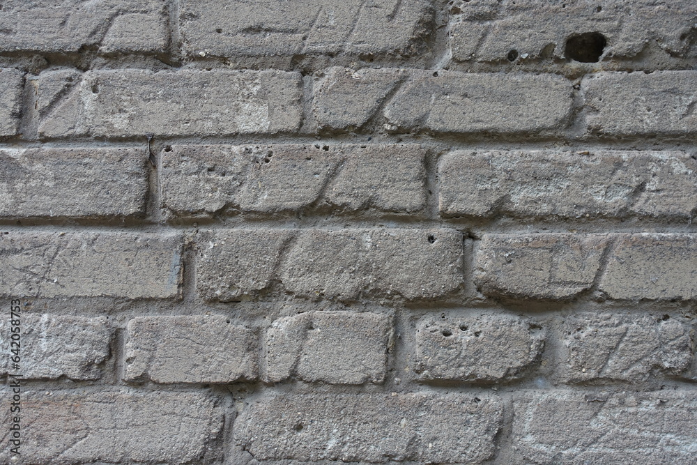 Uneven surface of old and scratched grey brick wall