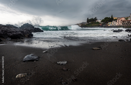 Waves hitting the shore on a cloudy overcast rainy stormy day. Cyclops Coast, black volcanic rocks and send on Sicily, near the town of Acireale photo