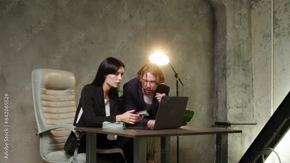 Portrait of a young woman and a business man sitting at a table late in the office in front of an open laptop and managing the company's finances and expenses. Portrait of a young woman and a business man sitting at a table late in the office in front of an open laptop and managing the company's finances and expenses.