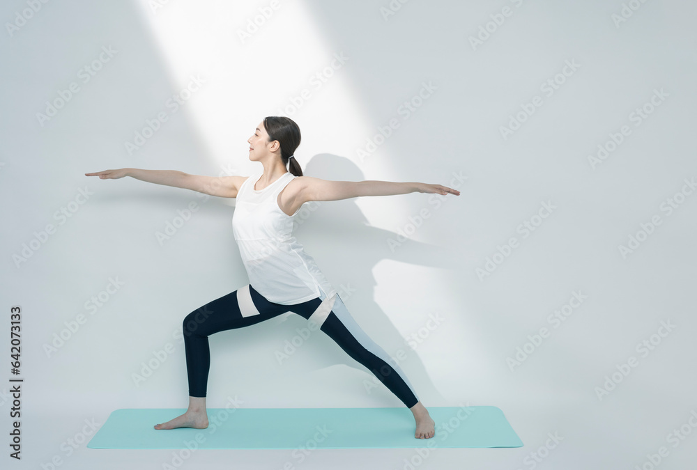 Fototapeta premium トレーニングウェアを着てヨガをする日本人女性/戦士のポーズ