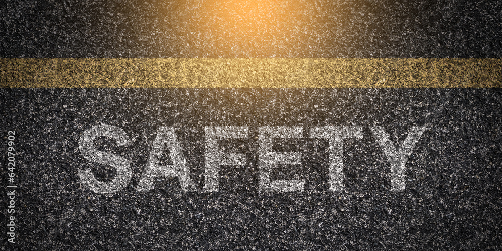 © Gabriele - Textured asphalt with 'Safety' text on the road under a yellow line, rough surface of tarmac with the word 'Safety' written, caution message on pavement, road safety concept