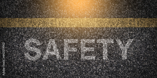 Textured asphalt with "Safety" text on the road under a yellow line, rough surface of tarmac with the word "Safety" written, caution message on pavement, road safety concept