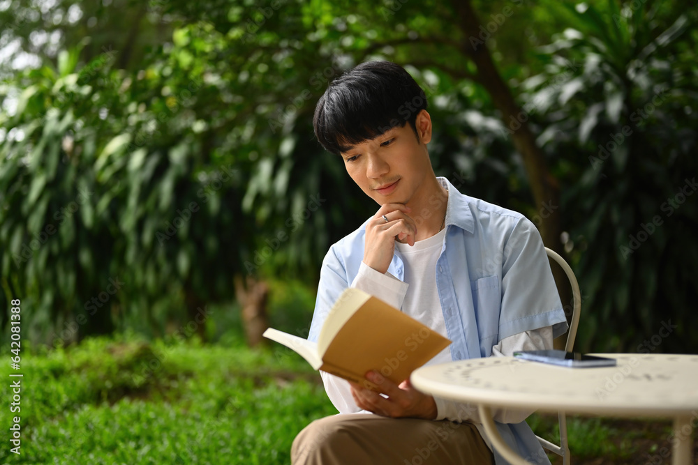Fototapeta premium A young Asian man reading a book while sitting in the garden