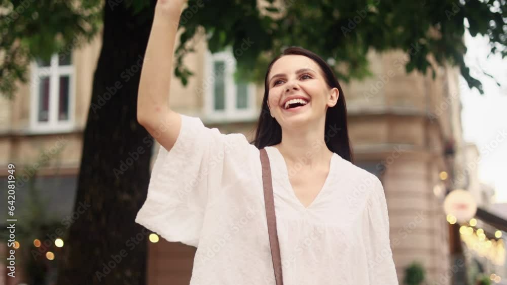 Portrait of happy smiling dark haired woman waiting to meet date and waving to someone at city centre Cute young girl say hello to someone after not seeing each other for long time outdoors Portrait of happy smiling dark haired woman waiting to meet date and waving to someone at city centre Cute young girl say hello to someone after not seeing each other for long time outdoors