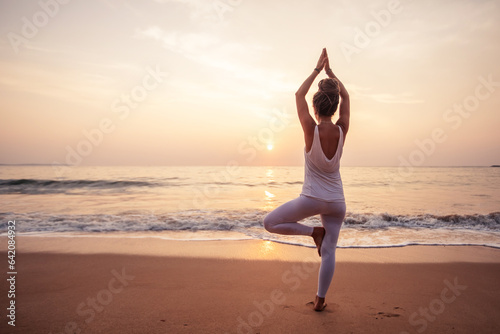 Woman practicing yoga by the ocean at dawn