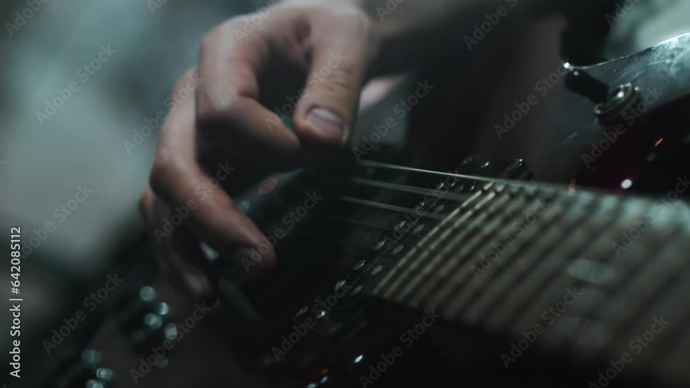Guitarist extract notes from the guitar hitting the strings with a pick while standing on a stage with the concert lighting during the show close up Guitarist extract notes from the guitar hitting the strings with a pick while standing on a stage with the concert lighting during the show close up
