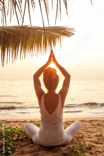 Woman practicing yoga by the ocean at dawn
